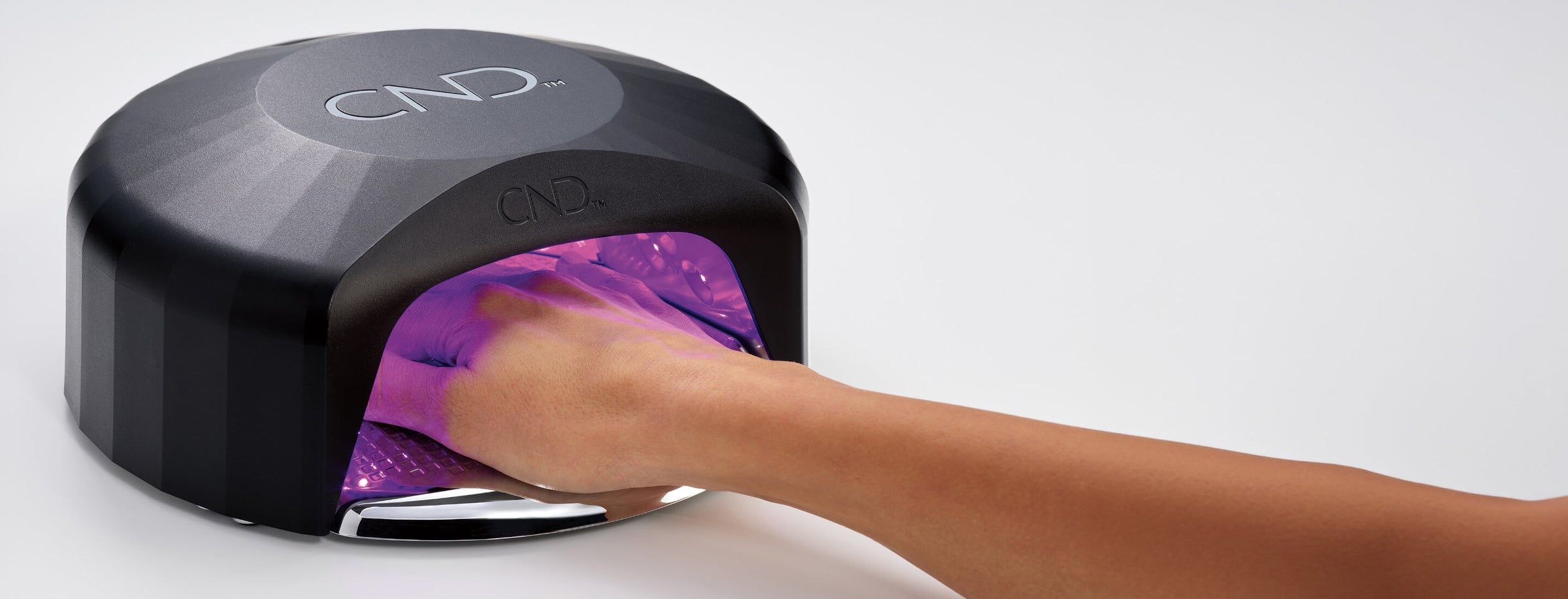 A black CND visible light lamp with a hand reaching inside to demonstrate the purple UV light, shown against a plain white background.